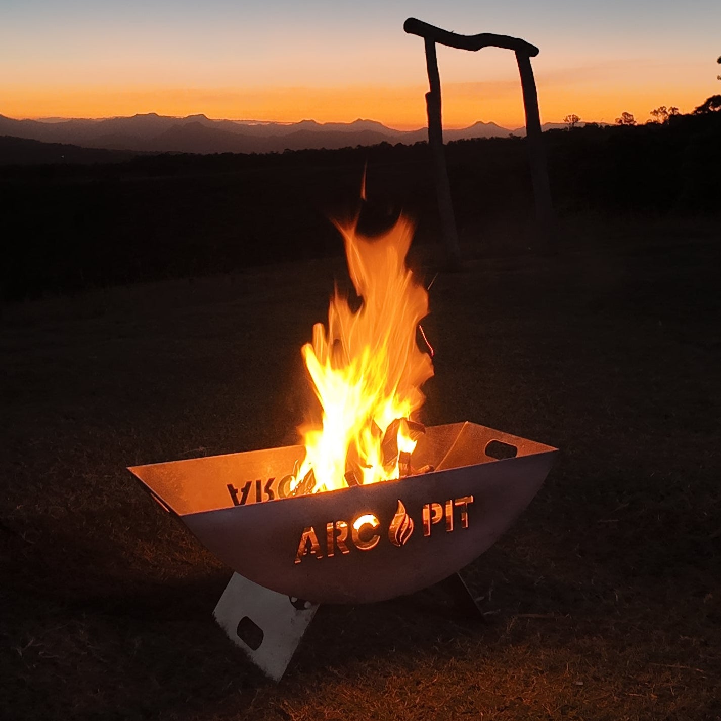 Fire pit with flames glowing in the dark, set against a sunset sky.